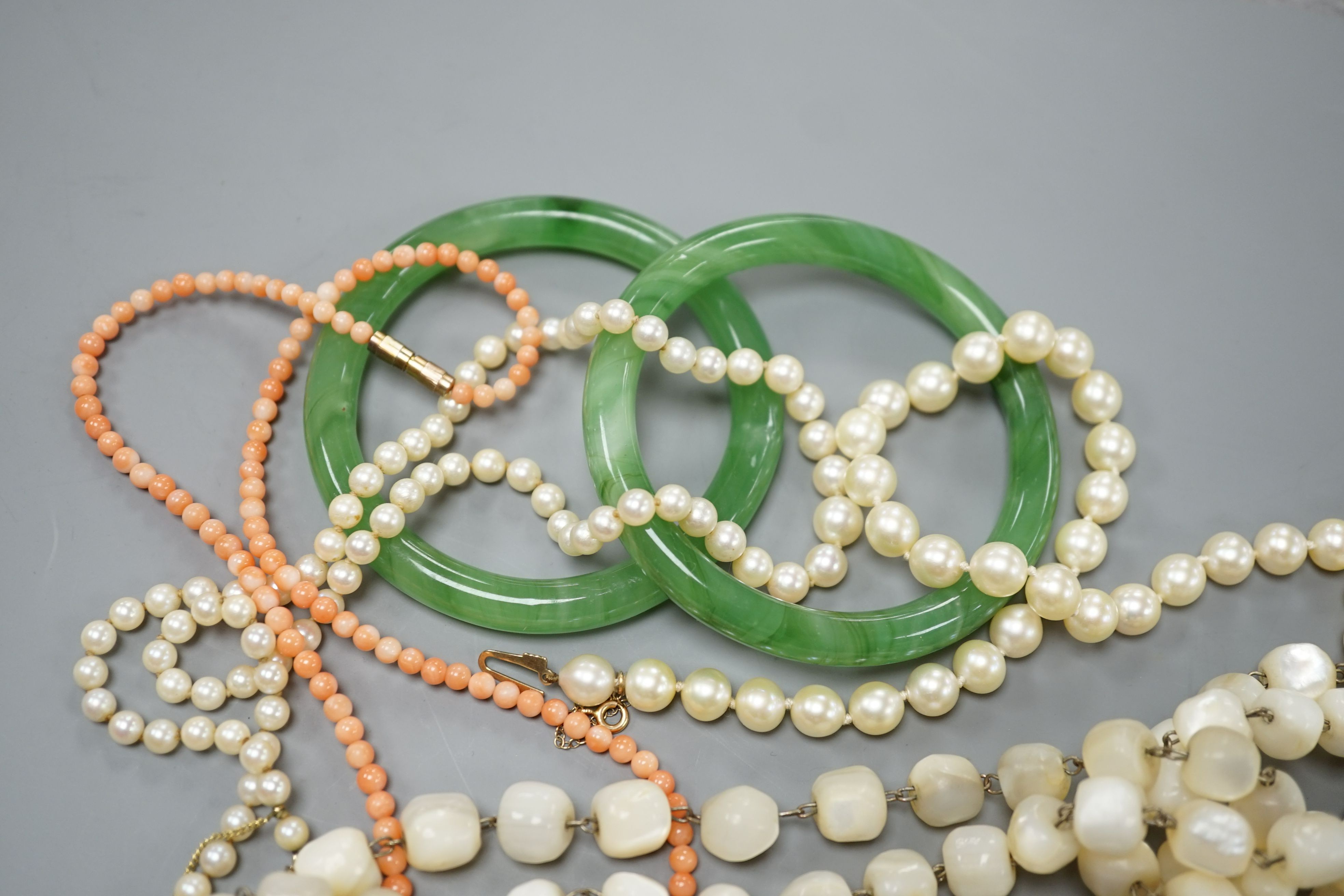 Two single strand cultured pearl necklaces, one with 9ct gold clasp, two green glass bangles, a coral bead necklace and a mother of pearl bead necklace.